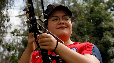 La deportista Mariana Zúñiga sonriendo, mientras sostiene su arco y vistiendo la camiseta del Team Chile.