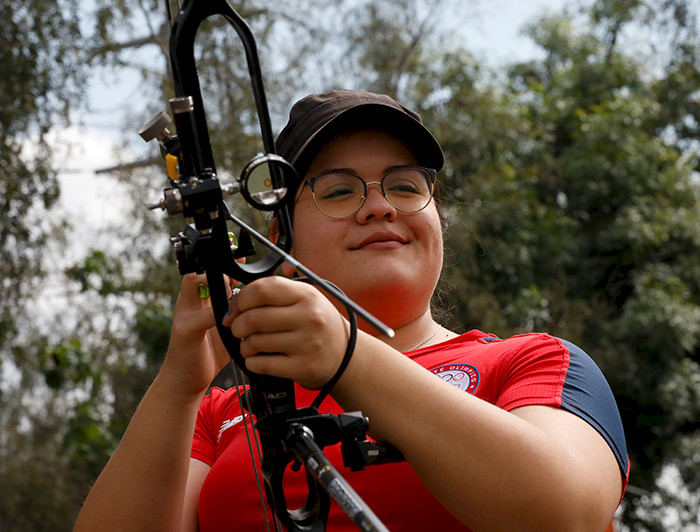 La deportista Mariana Zúñiga sonriendo, mientras sostiene su arco y vistiendo la camiseta del Team Chile.