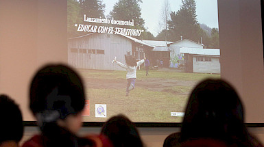 Pantalla que muestra la imagen del documental mientras el público la observa.