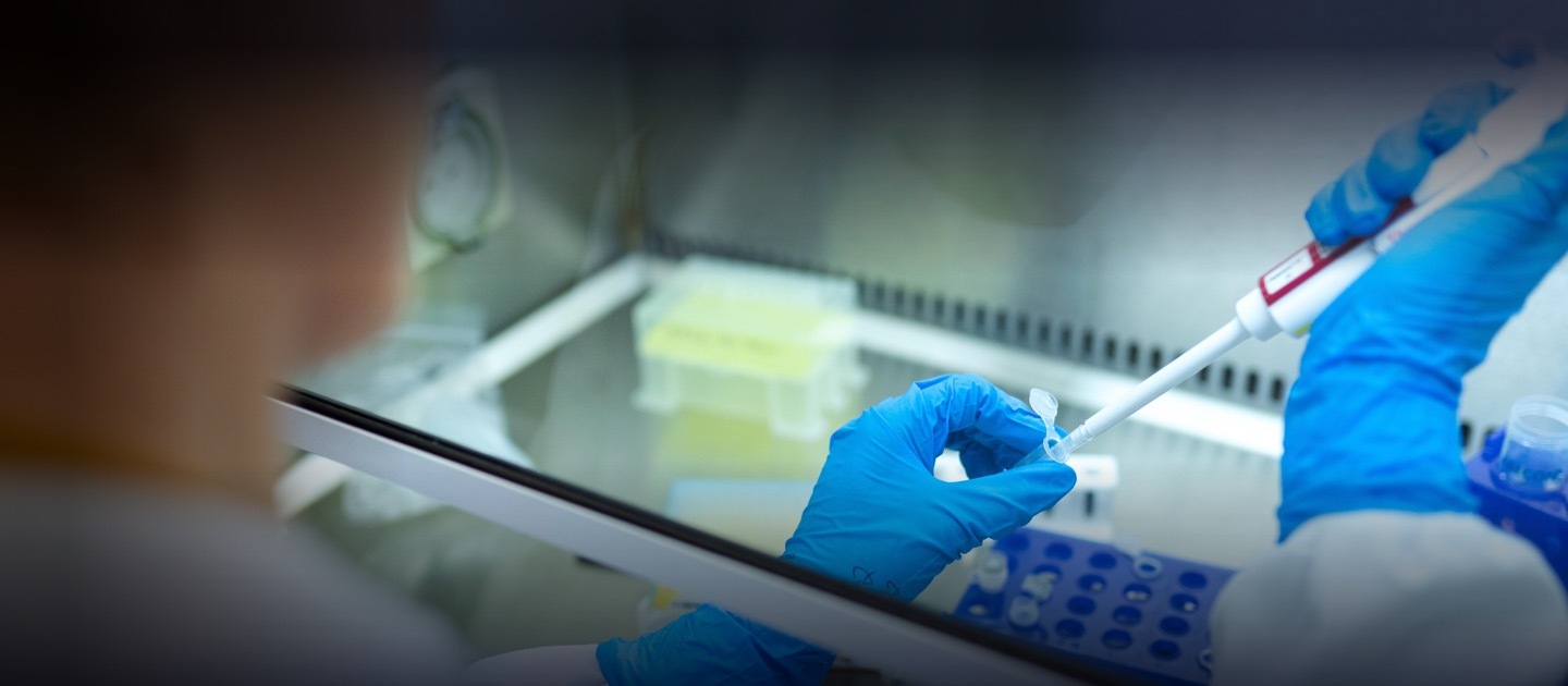 Silueta de una personas y sus manos con guantes azules haciendo un experimento en un laboratorio.