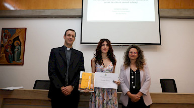 tres personas de pie, una de ellas sostiene un diploma