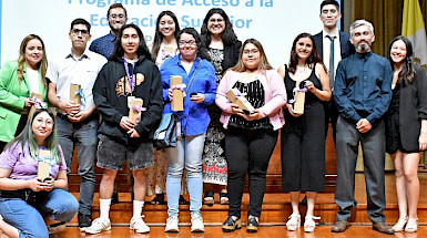 Grupo de jóvenes reconocidos por el programa PACE arriba de un escenario y sosteniendo un presente.