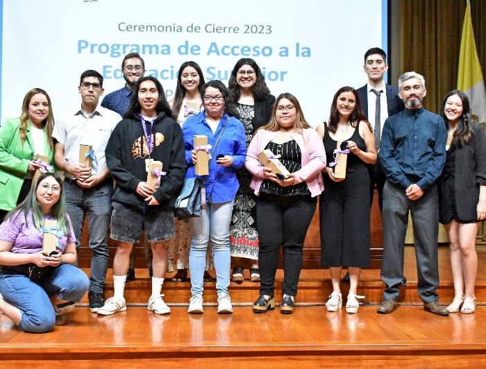 Grupo de jóvenes reconocidos por el programa PACE arriba de un escenario y sosteniendo un presente.