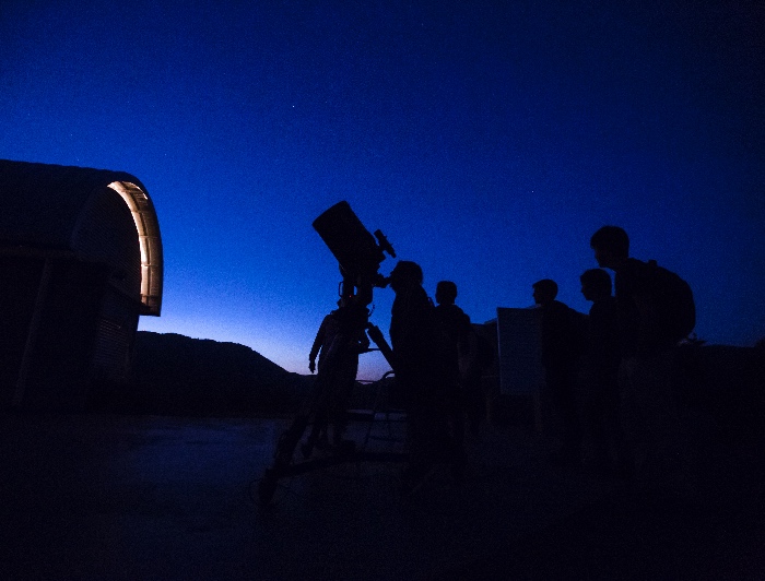 Personas observan un telescopio en la oscuridad.