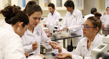 Investigadoras trabajando con unos tubos de ensayo en un laboratorio, usando delantal blanco.