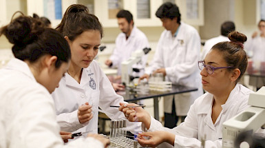 Investigadoras trabajando con unos tubos de ensayo en un laboratorio, usando delantal blanco.