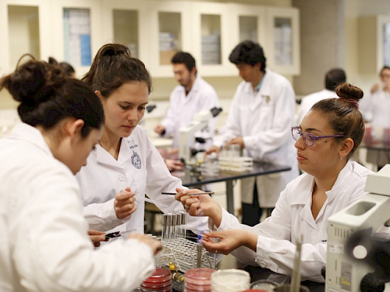 Investigadoras trabajando con unos tubos de ensayo en un laboratorio, usando delantal blanco.