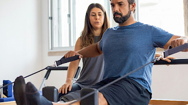 Hombre en ropa deportiva haciendo ejercicios con una mujer que lo observa al lado.