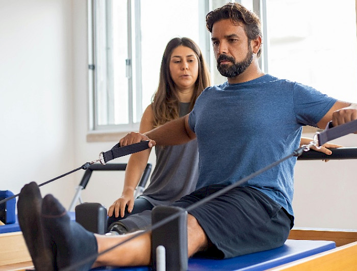 Hombre en ropa deportiva haciendo ejercicios con una mujer que lo observa al lado.
