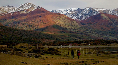 Dos personas caminan por un área rural con las montañas de fondo en Isla Navarino.