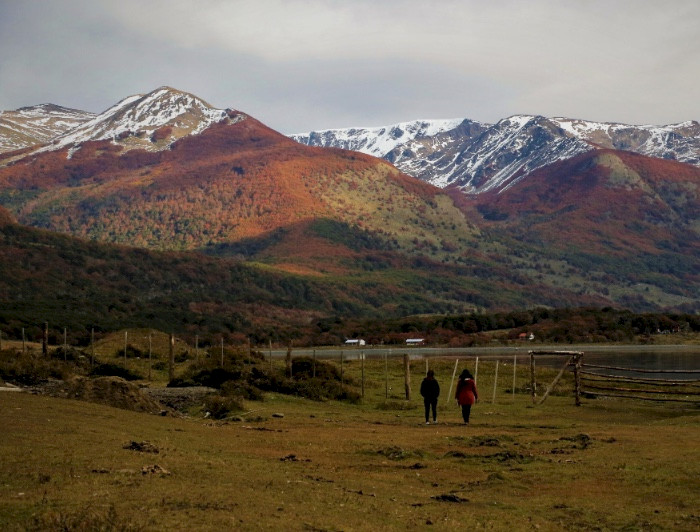 Dos personas caminan por un área rural con las montañas de fondo en Isla Navarino.