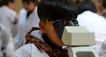 Niño usando un delantal blanco observando por microscopio.