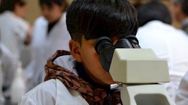 Niño usando un delantal blanco observando por microscopio.