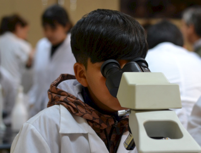 Niño usando un delantal blanco observando por microscopio.