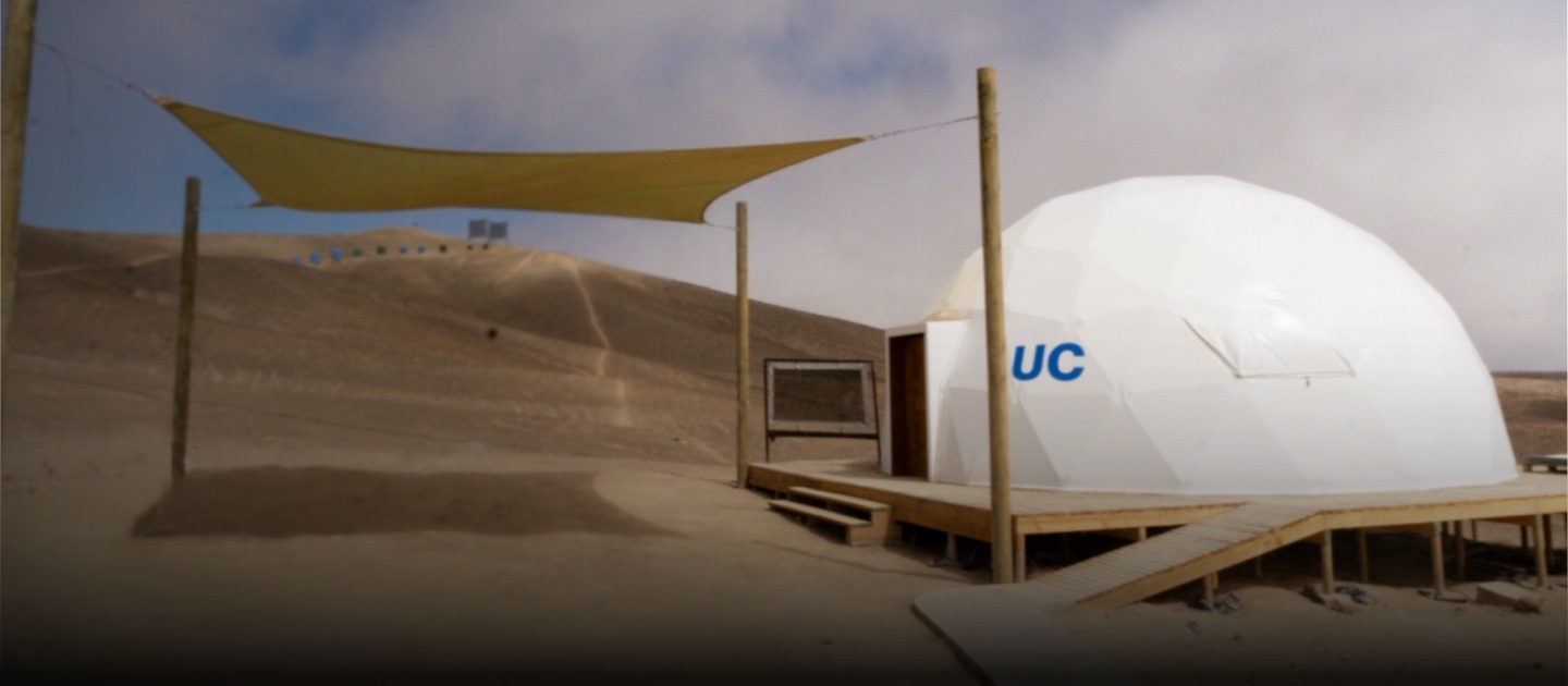 White dome with blue UC Chile logo, along with a scale fog catcher, a shaded patio and fog catcher in the background.