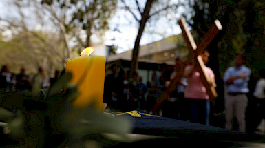 vela sobre un altar y de fondo, una persona llevando una cruz grande de madera