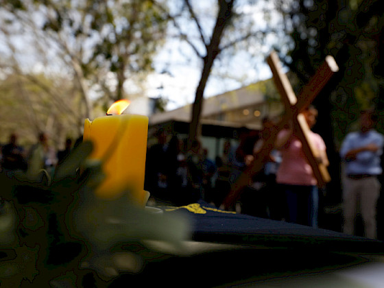 vela sobre un altar y de fondo, una persona llevando una cruz grande de madera