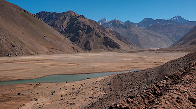 Un curso de agua con escasez hídrica en medio de tierra seca y montañas de fondo.