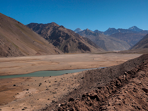 Un curso de agua con escasez hídrica en medio de tierra seca y montañas de fondo.