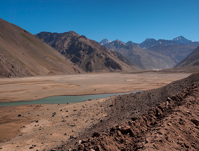 Un curso de agua con escasez hídrica en medio de tierra seca y montañas de fondo.