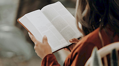 Mujer, que se encuentra de espaldas, sostiene un libro abierto.