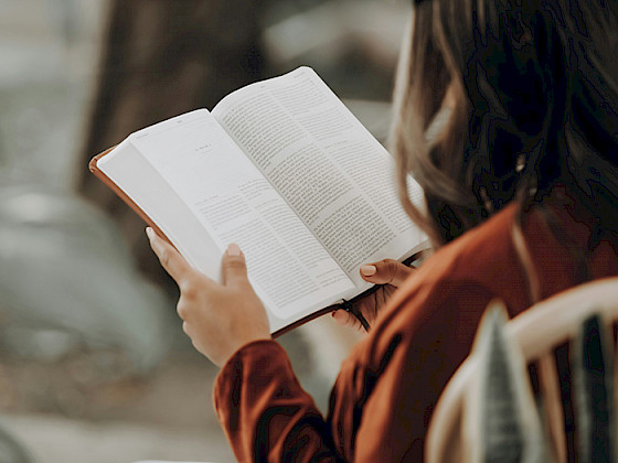 Mujer, que se encuentra de espaldas, sostiene un libro abierto.