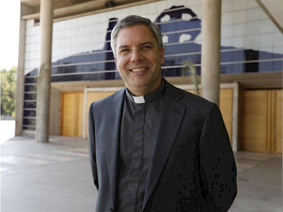 Hombre adulto de pie con una iglesia a sus espaldas