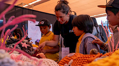 La investigadora de Núcleo NUTME, Celeste Kroeger, le muestra a unos niños la exposición Tramares, Tejiendo Arrecifes.