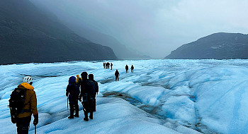 Grupo de personas sobre un glaciar con montañas de fondo.