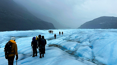 Grupo de personas sobre un glaciar con montañas de fondo.