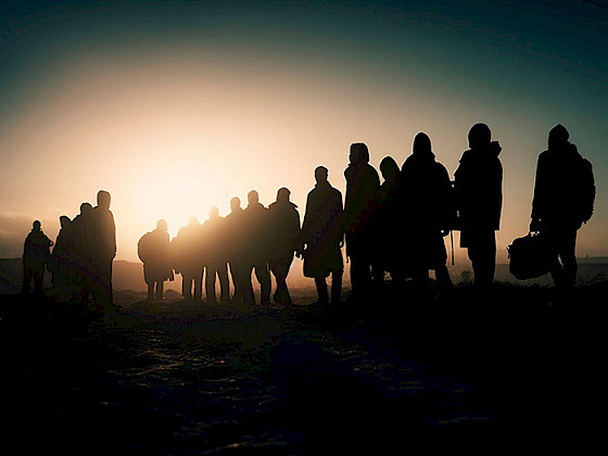 Siluetas de migrantes caminando al atardecer.