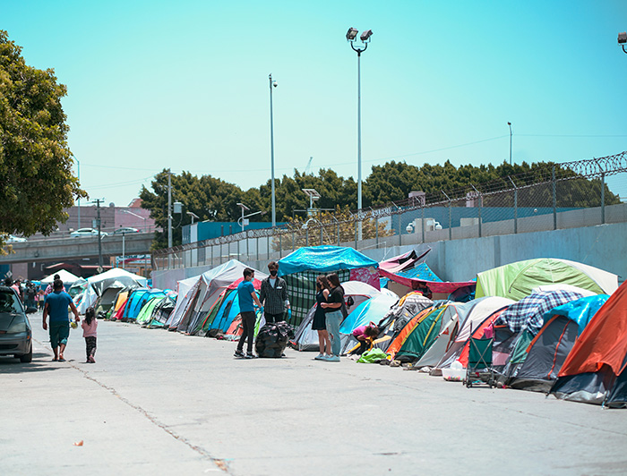 Carpas de migrantes en una calle al lado de un muro.