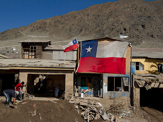 Vivienda semi destruida por lodo, con una bandera chilena