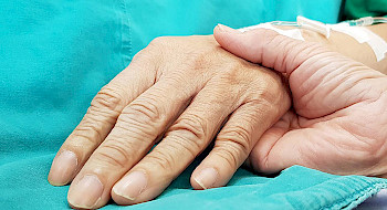 Una mano sostiene la de una persona enferma.