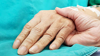 Una mano sostiene la de una persona enferma.
