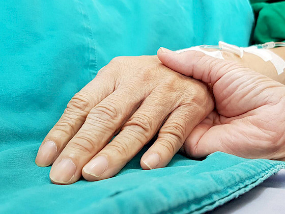 Una mano sostiene la de una persona enferma.
