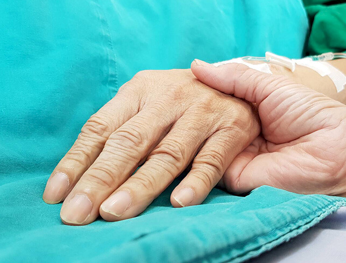 Una mano sostiene la de una persona enferma.