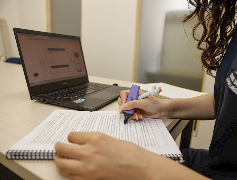 Estudiante con destacador y un texto frente a un computador 