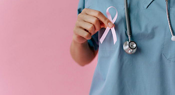 persona sin rostro, con ropa clínica celeste, sostiene lazo rosa