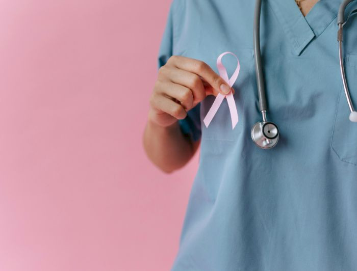 persona sin rostro, con ropa clínica celeste, sostiene lazo rosa