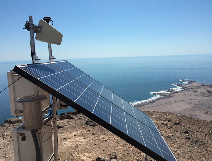 Panel solar, de fondo un paisaje árido y el océano Pacífico.