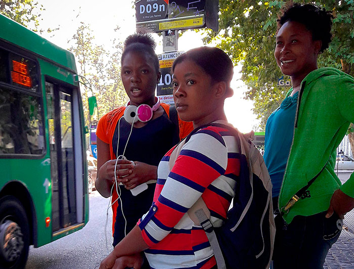 Tres jóvenes migrantes en un paradero de buses.
