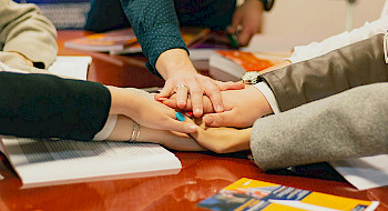 Manos apiladas simbolizando colaboración.