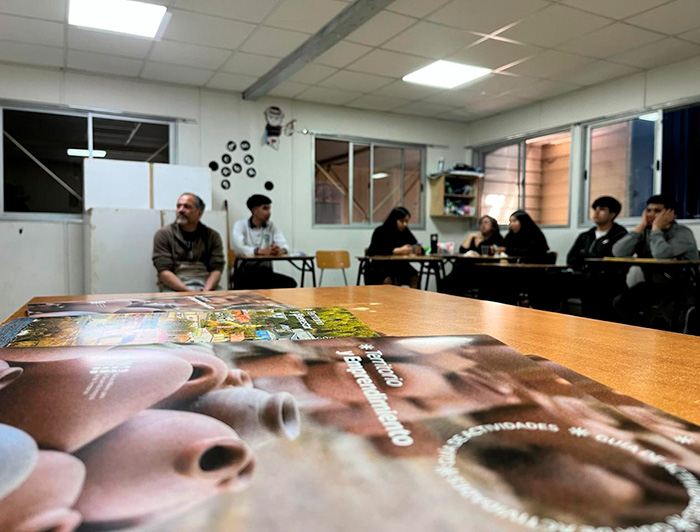Guías de actividades en primer plano, de fondo un profesor y sus estudiantes en una sala de clases.