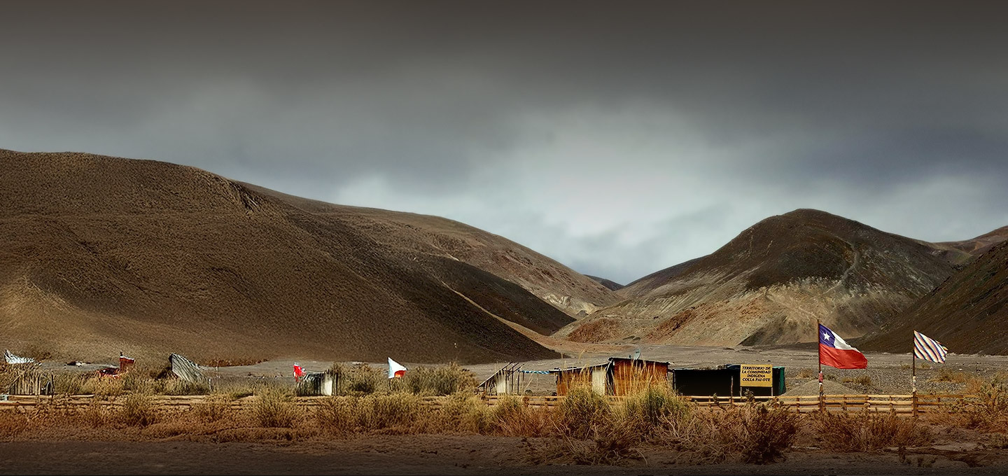 Viviendas rurales junto a una bandera chilena con montañas de fondo.