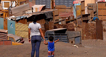 Mujer joven junto a un niño de espaldas observando un campamento.