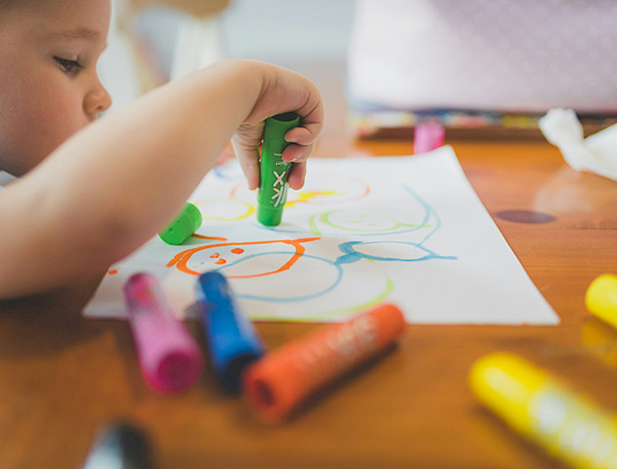 Niño dibuja con unos crayones sobre un papel