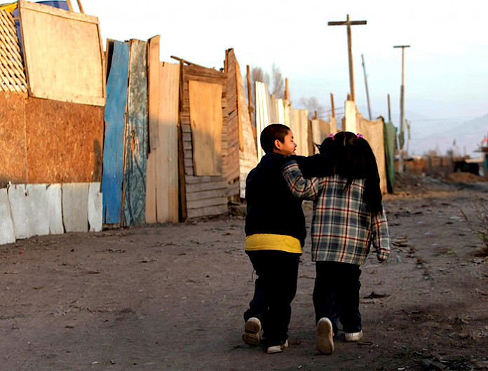 Niños caminan abrazados por una calle de tierra en un campamento