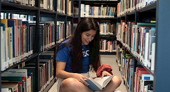 Joven leyendo un libro en una biblioteca