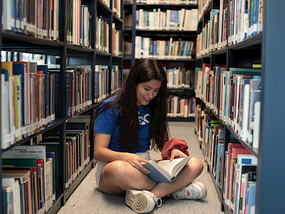 Joven leyendo un libro en una biblioteca